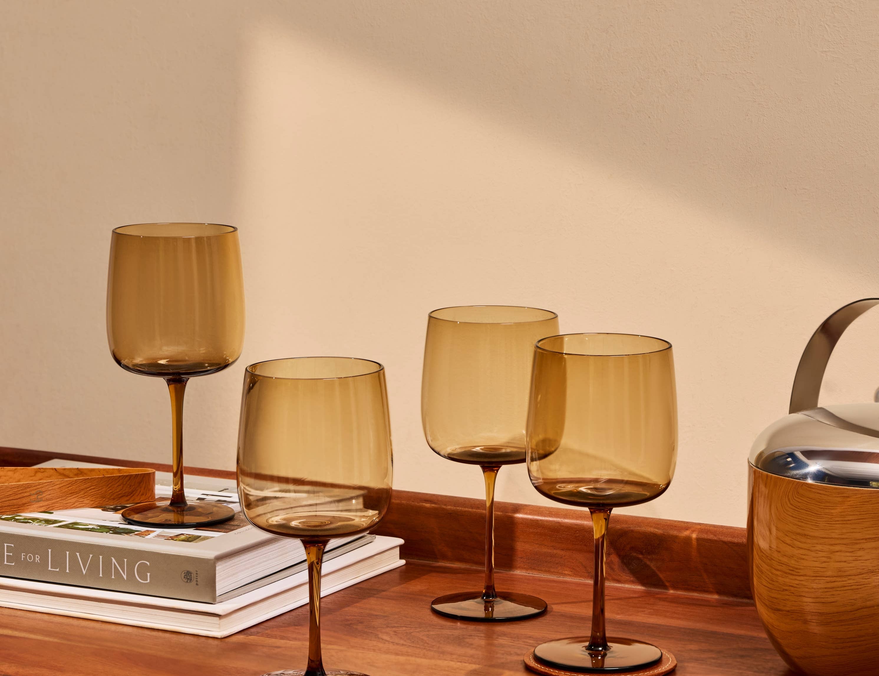 The Collective Ember Wine Glasses Set of 4 in amber glass on a wooden table beside books