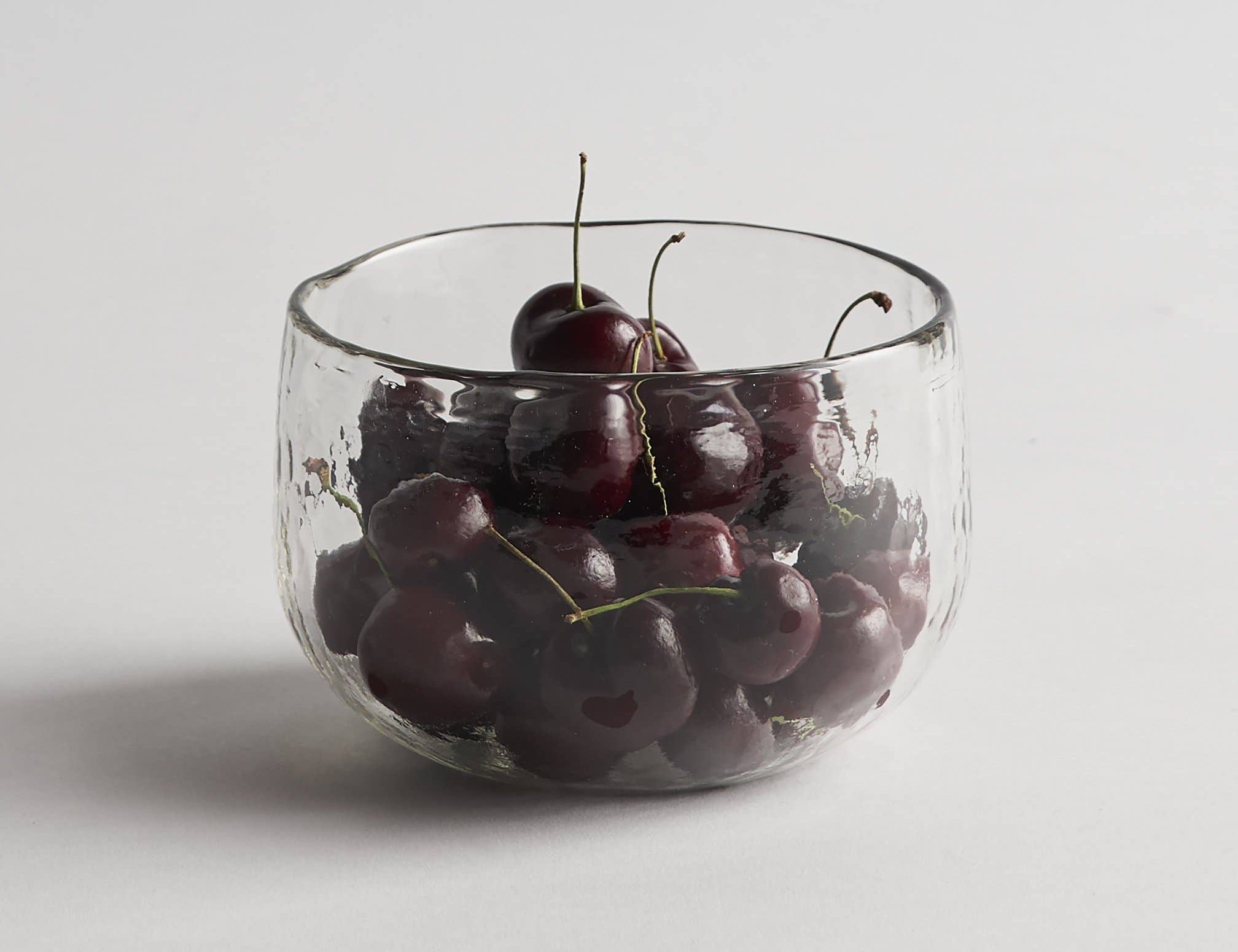 The Collective Pebbled Bowls Set of 2, a textured glass bowl filled with cherries