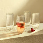 The Collective Pebbled Large Glasses Set of 4 lined up on a sunlit ledge, one with a rose drink