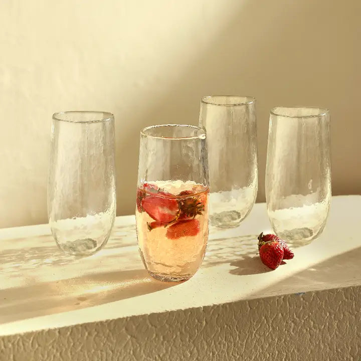 The Collective Pebbled Large Glasses Set of 4 lined up on a sunlit ledge, one with a rose drink