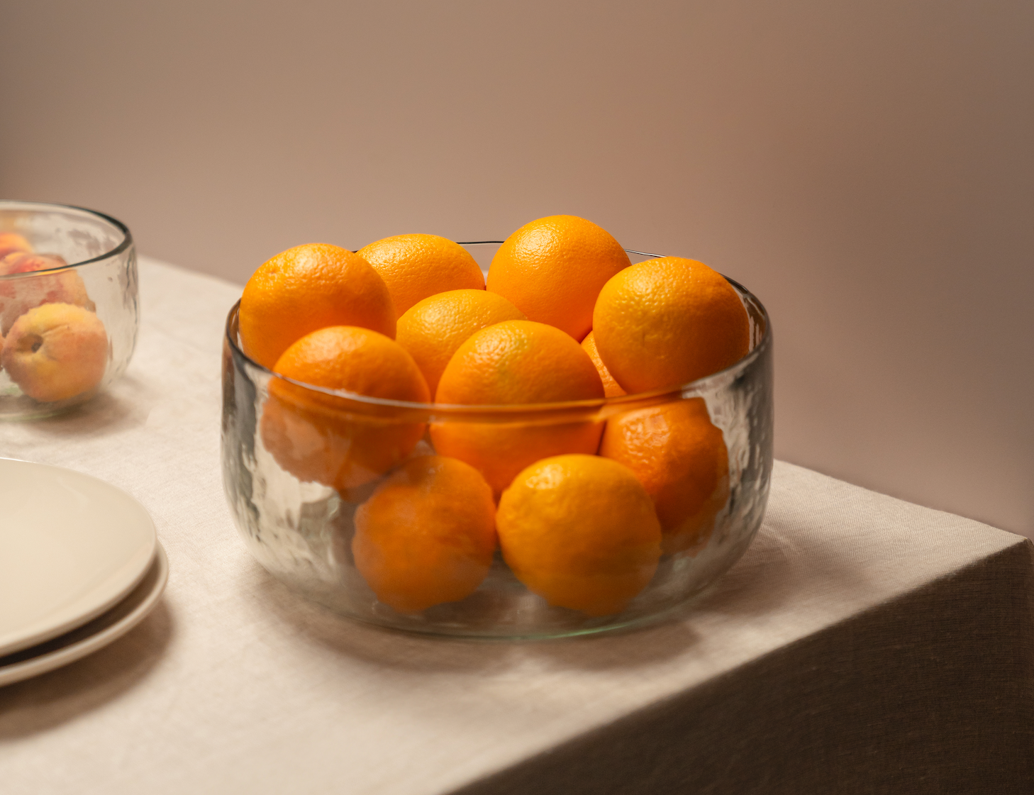 The Collective Pebbled Salad Bowl filled with oranges on a table with stacked plates
