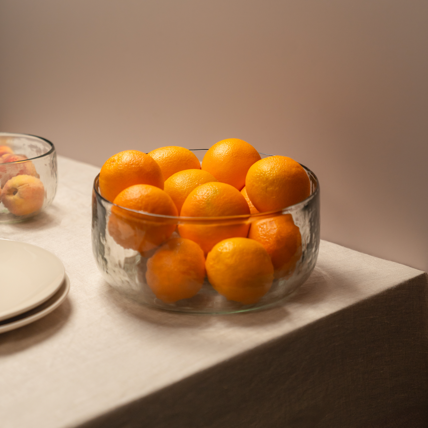 The Collective Pebbled Salad Bowl filled with oranges on a table with stacked plates