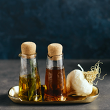 The Collective Pebbled Small Carafes Set of 2 with cork stoppers holding oil and vinegar on a brass tray