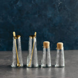 The Collective Pebbled Small Carafes and shakers with cork stoppers and gold spoons on a dark surface