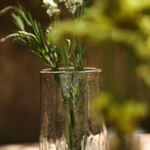 The Collective Pebbled Tall Vase holding greenery and small white flowers outdoors