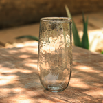 The Collective Pebbled Tall Vase, a slim textured glass vase on a wooden table in dappled light