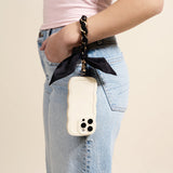 Woman in jeans carrying a phone on her wrist with The Darling Effect Phone Scarf in Black