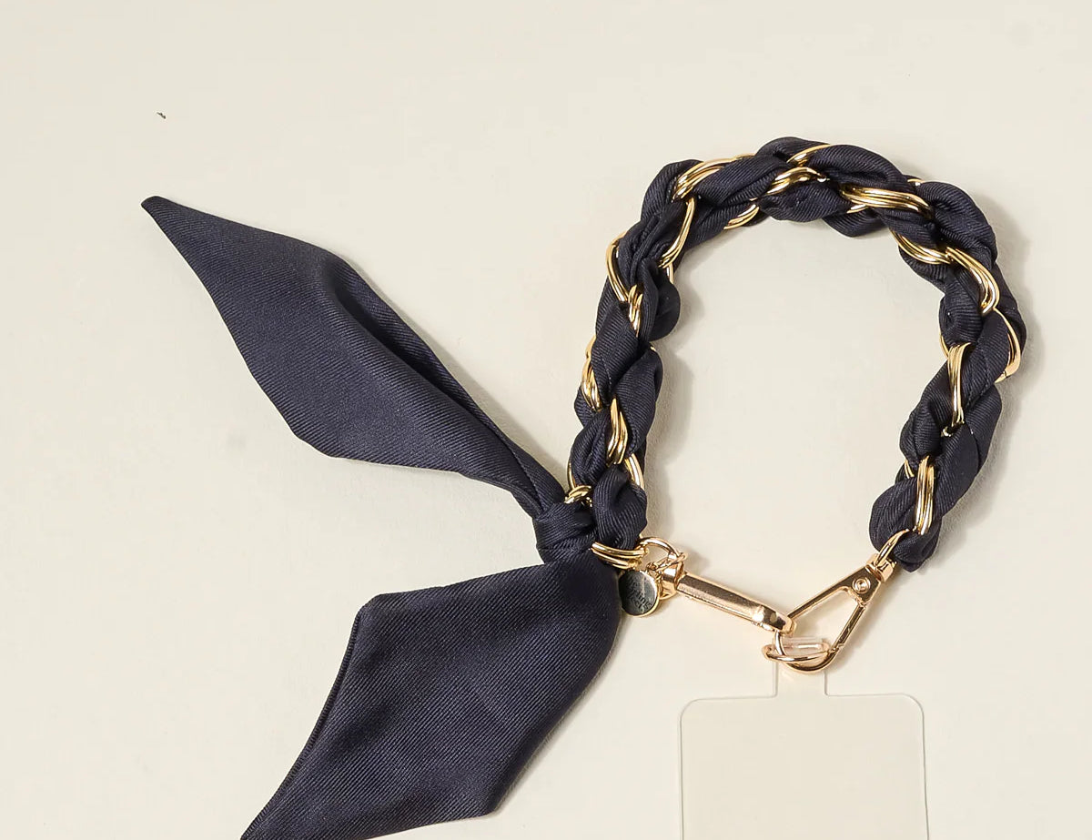 The Darling Effect Phone Scarf in Black, a satin scarf braided through a gold chain wristlet with a phone tether tab