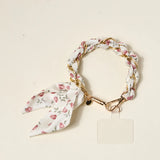The Darling Effect Phone Scarf in Garden Party, a cream floral satin scarf braided through a gold chain wristlet