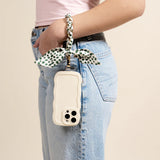 Woman in jeans carrying a phone on her wrist with The Darling Effect Phone Scarf in Olive Dot