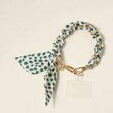 The Darling Effect Phone Scarf in Olive Dot, a white satin scarf with green dots on a gold chain wristlet