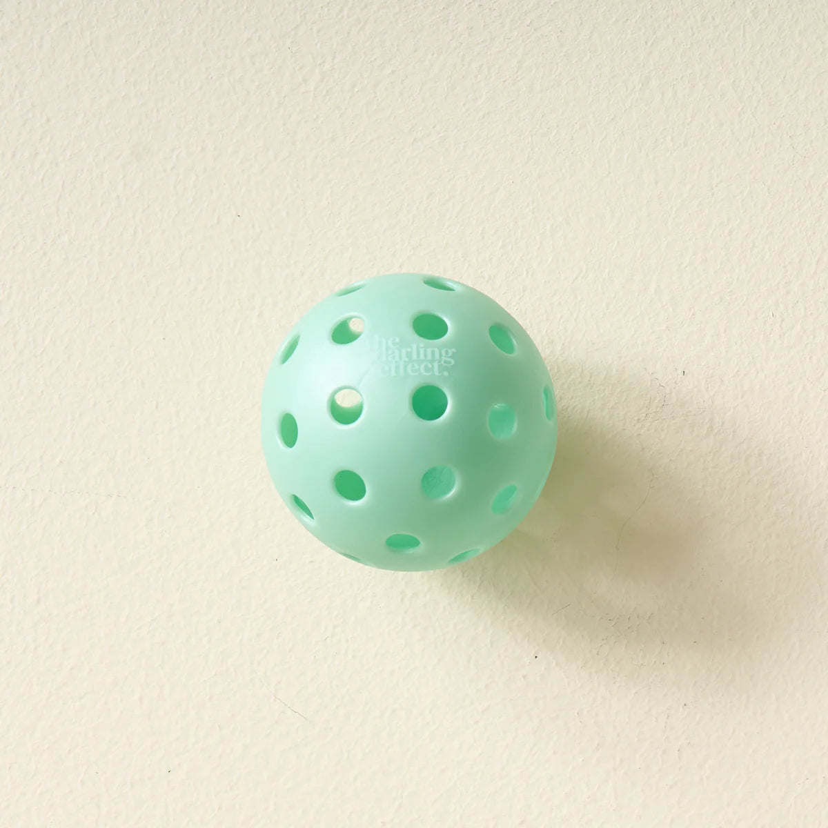 Single aqua pickleball from The Darling Effect Pickleball Ball Set on a cream background