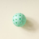 Single aqua pickleball from The Darling Effect Pickleball Ball Set on a cream background