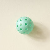Single aqua pickleball from The Darling Effect Pickleball Ball Set on a cream background