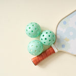 Aqua pickleballs from The Darling Effect Pickleball Ball Set grouped by a daisy paddle handle