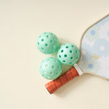 Aqua pickleballs from The Darling Effect Pickleball Ball Set grouped by a daisy paddle handle