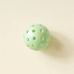Single mint green pickleball from The Darling Effect Pickleball Ball Set on a cream background