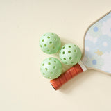 Three green pickleballs from The Darling Effect Pickleball Ball Set beside a floral paddle