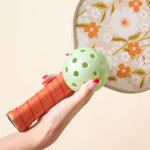 Hand holding a floral paddle and a green pickleball from The Darling Effect Pickleball Ball Set