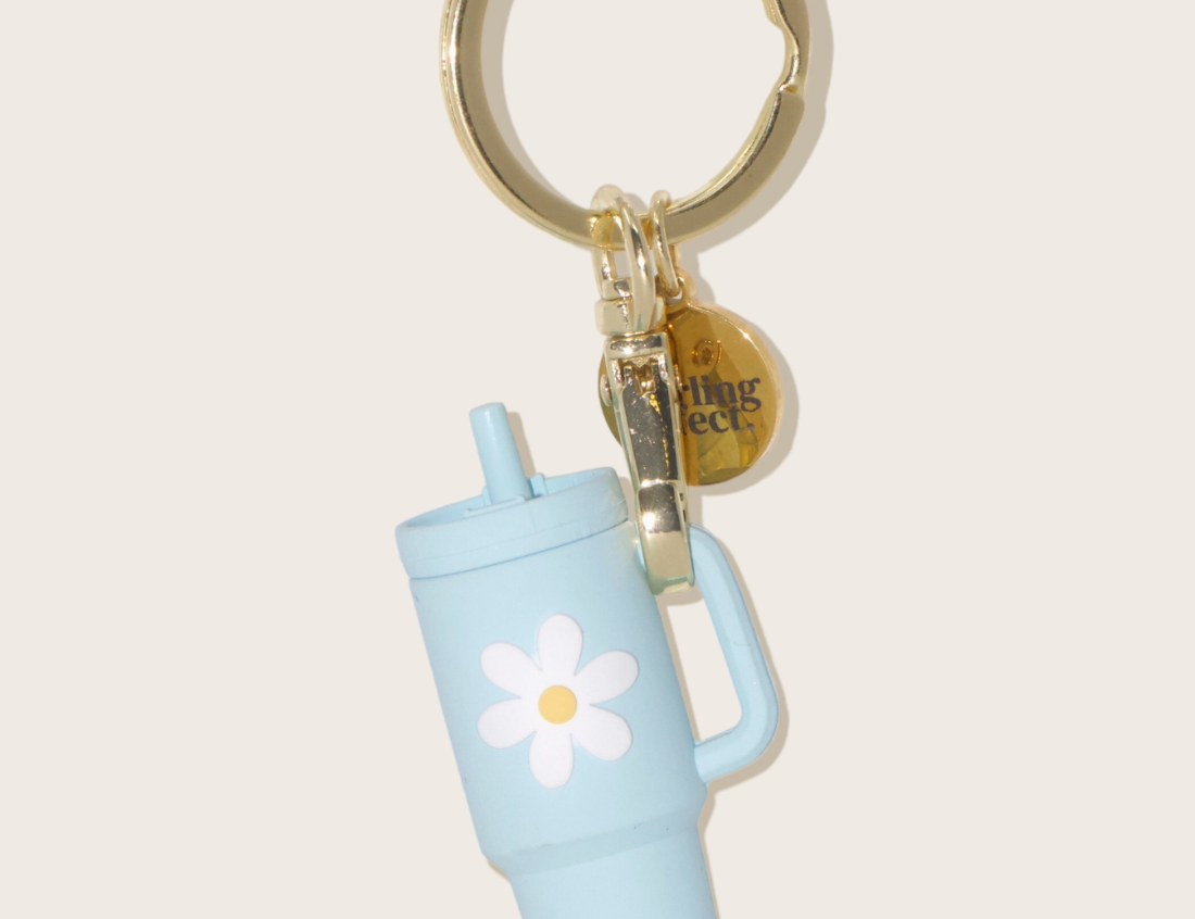 The Darling Effect Tiny Tumbler Keychain, a miniature light blue tumbler with a daisy on a gold ring