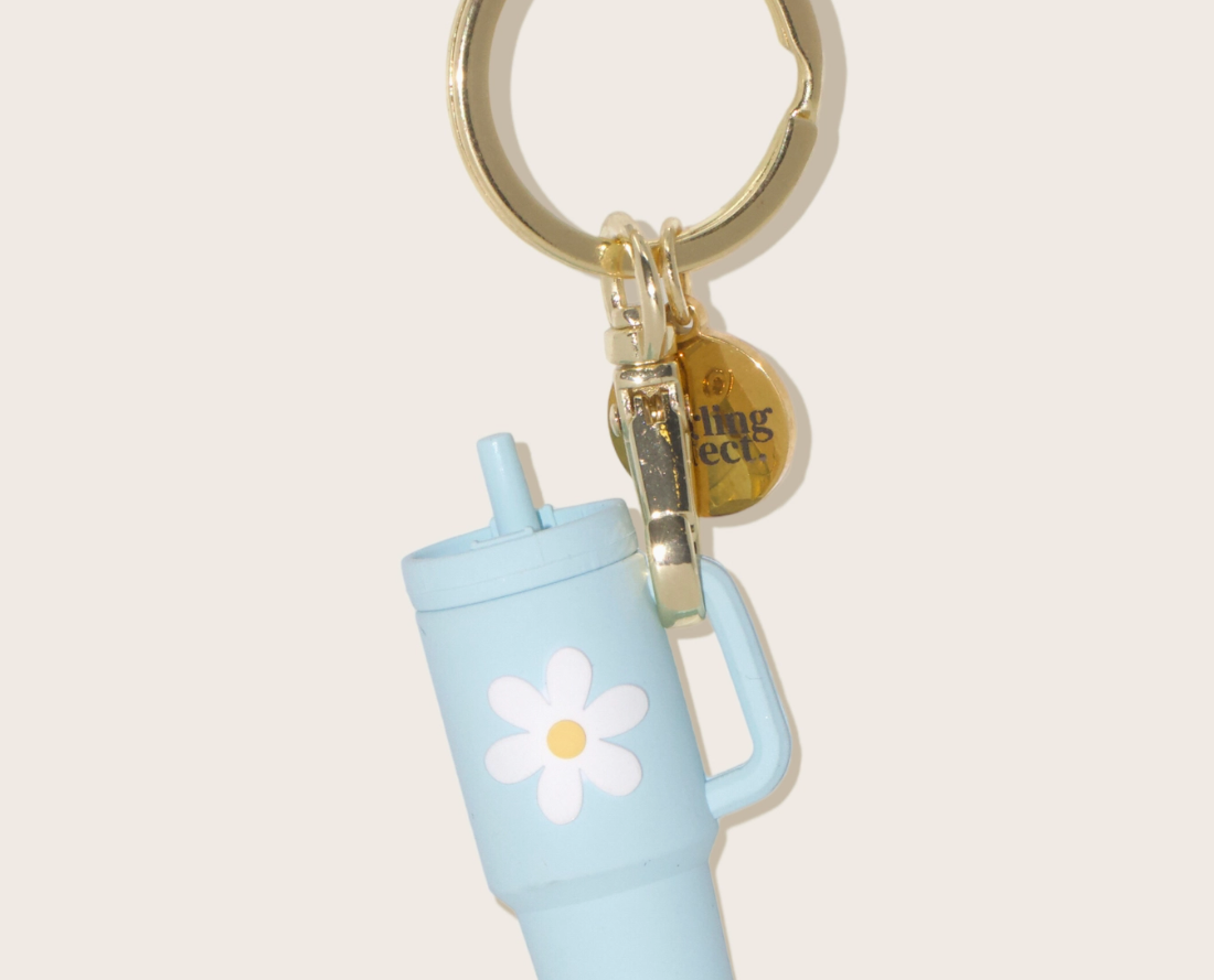 The Darling Effect Tiny Tumbler Keychain, a miniature light blue tumbler with a daisy on a gold ring