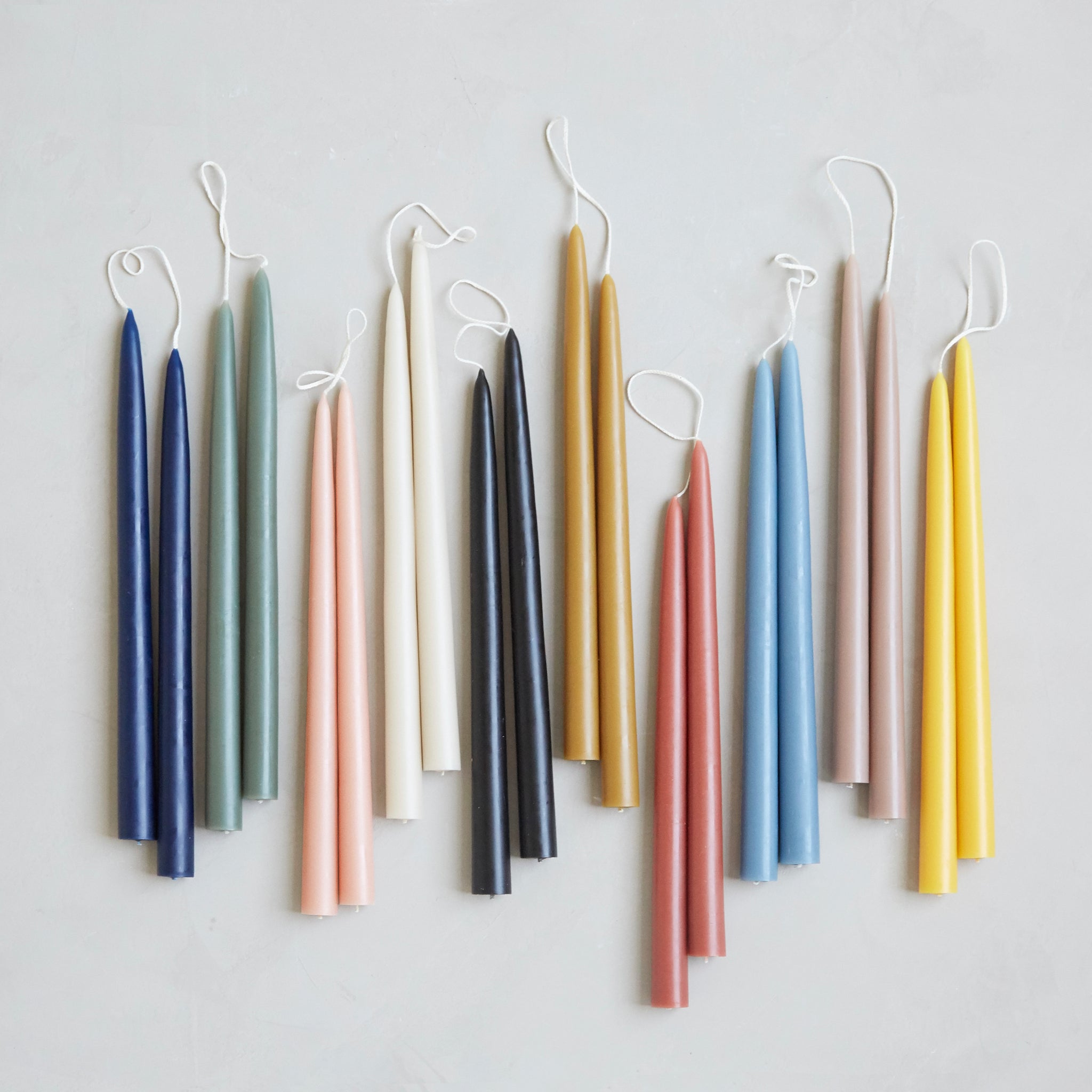 The Floral Society 18-inch Dipped Taper Candles, pairs in navy, sage, ivory, blush, terracotta, honey, black and yellow hanging by their wicks on a neutral background