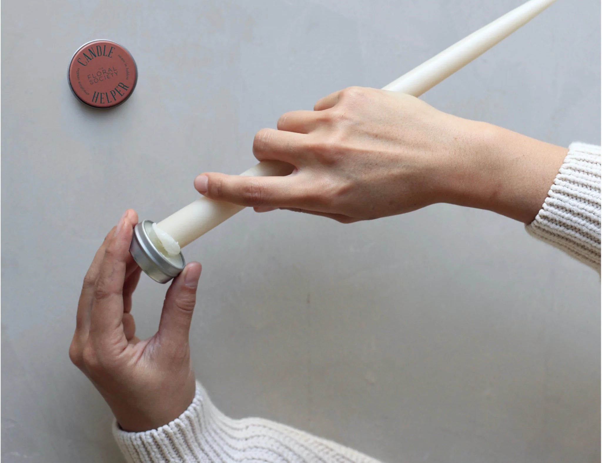 Hands applying The Floral Society Candle Helper wax to the base of a white taper candle