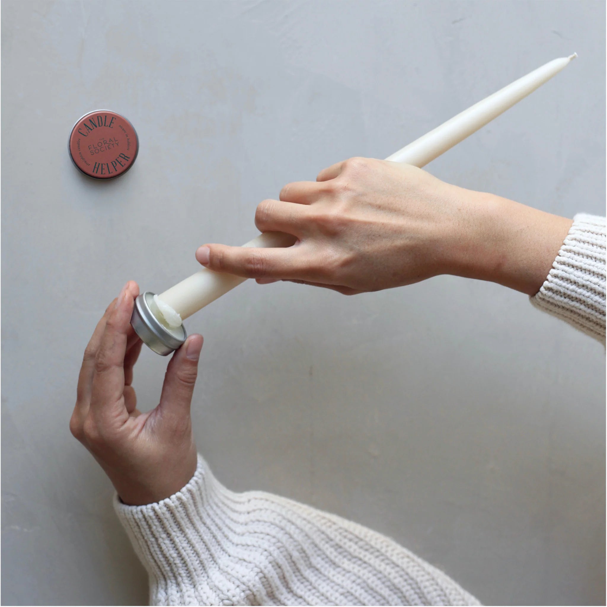 Hands applying The Floral Society Candle Helper wax to the base of a white taper candle
