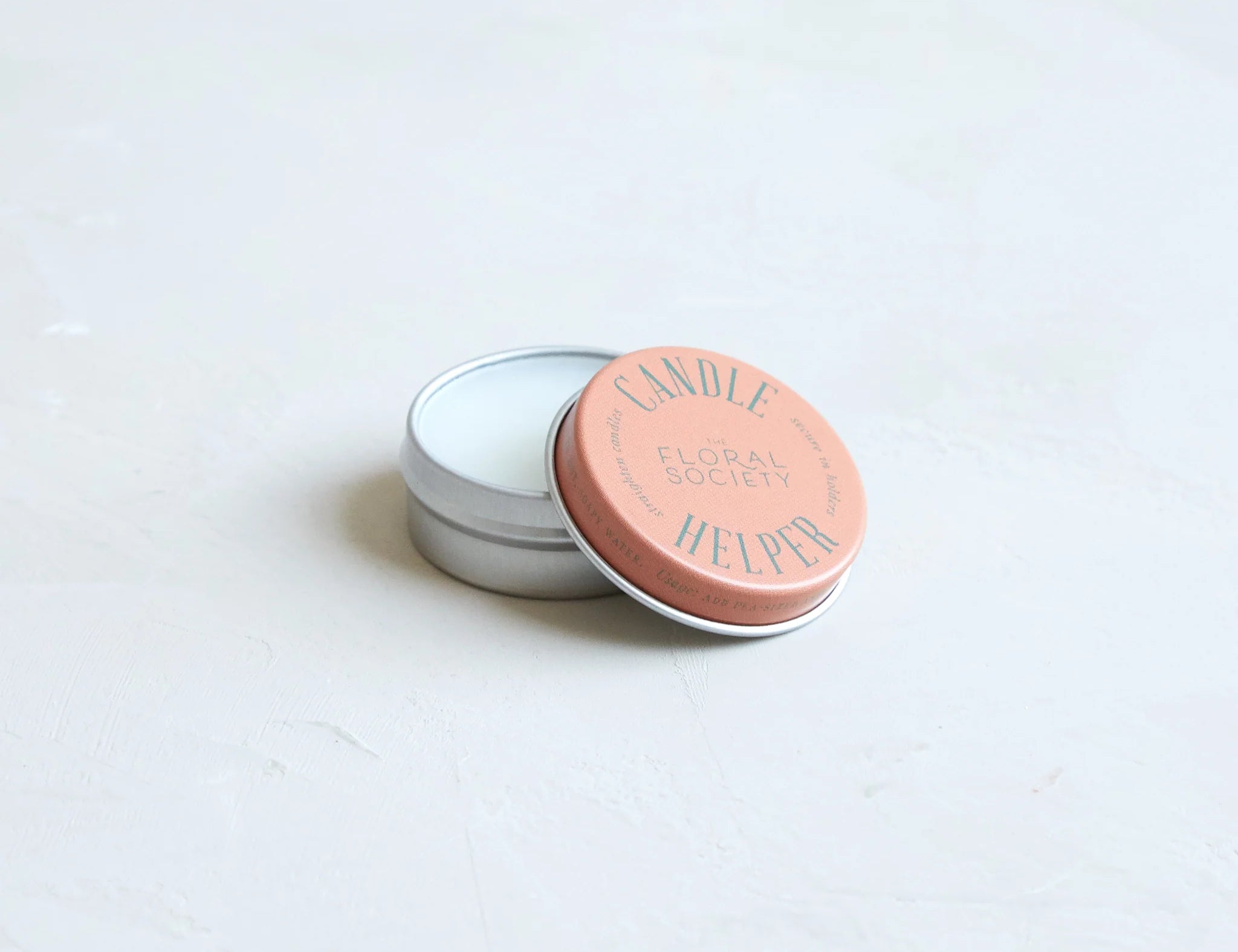 The Floral Society Candle Helper, a small silver tin of wax adhesive with a terracotta lid