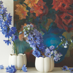 The Floral Society Ceramic Flower Frog Vases holding blue delphinium in front of a floral painting