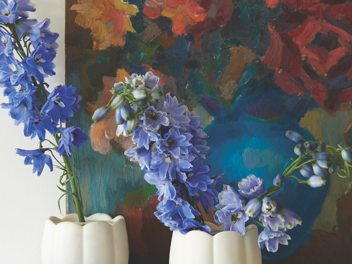 The Floral Society Ceramic Flower Frog Vases holding blue delphinium in front of a floral painting