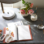 The Floral Society Ceramic Flower Frog Vases with roses on a slate desk with a sketchbook and scissors