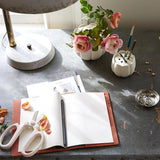 The Floral Society Ceramic Flower Frog Vases with roses on a slate desk with a sketchbook and scissors