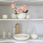 The Floral Society Ceramic Flower Frog Vases with pink roses on white shelves beside glass bottles