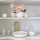 The Floral Society Ceramic Flower Frog Vases with pink roses on white shelves beside glass bottles