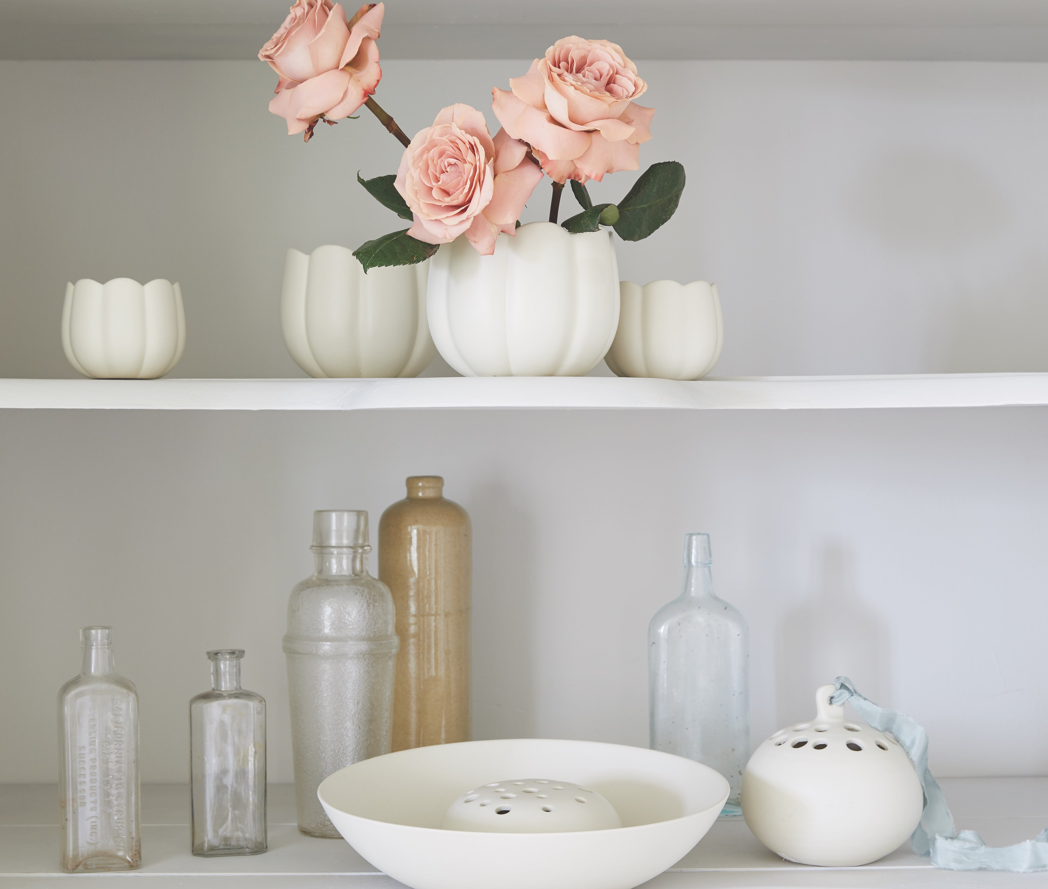 The Floral Society Ceramic Flower Frog Vases with pink roses on white shelves beside glass bottles
