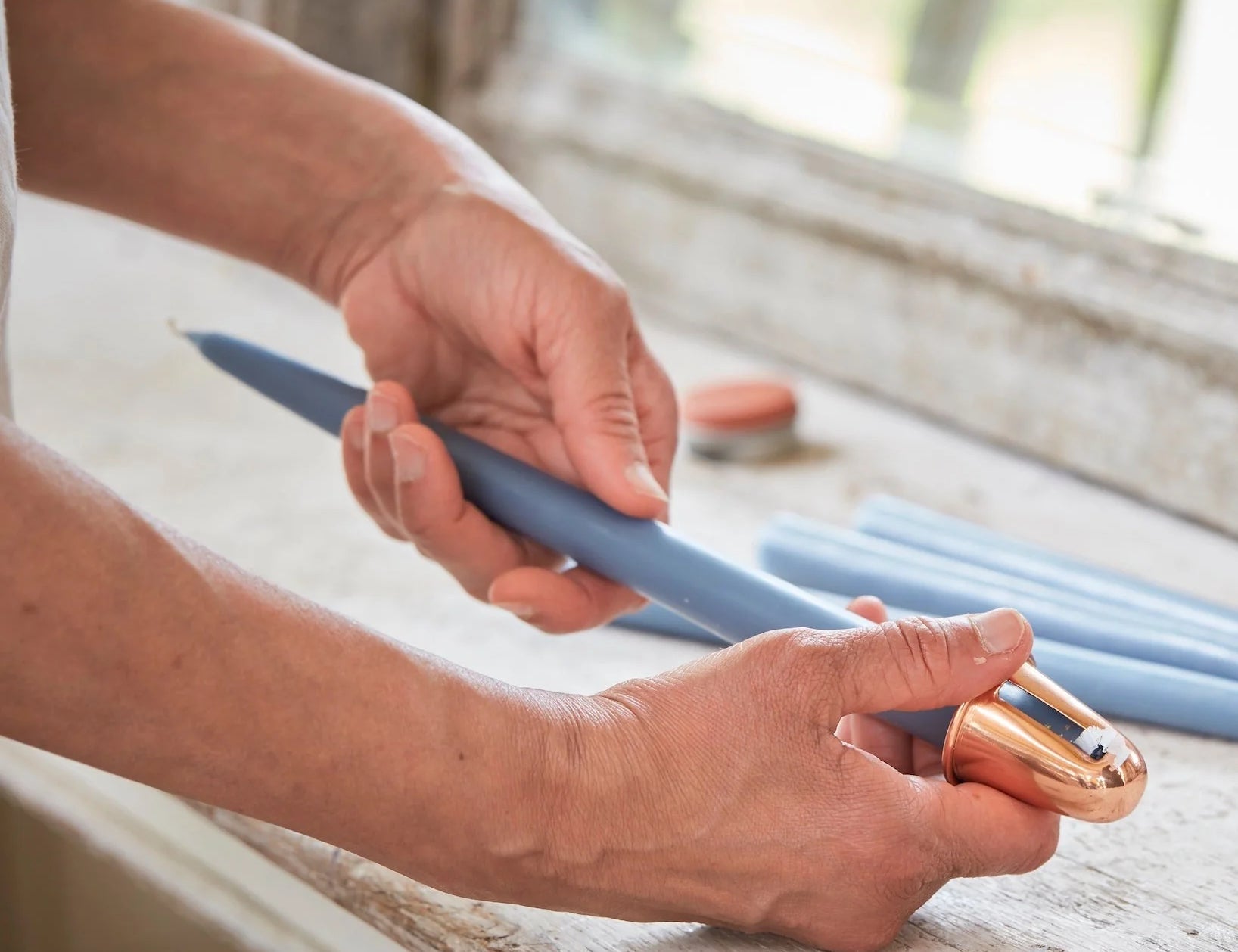 Hands using The Floral Society Copper Candle Sharpener on a blue taper candle