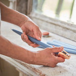 Hands using The Floral Society Copper Candle Sharpener on a blue taper candle