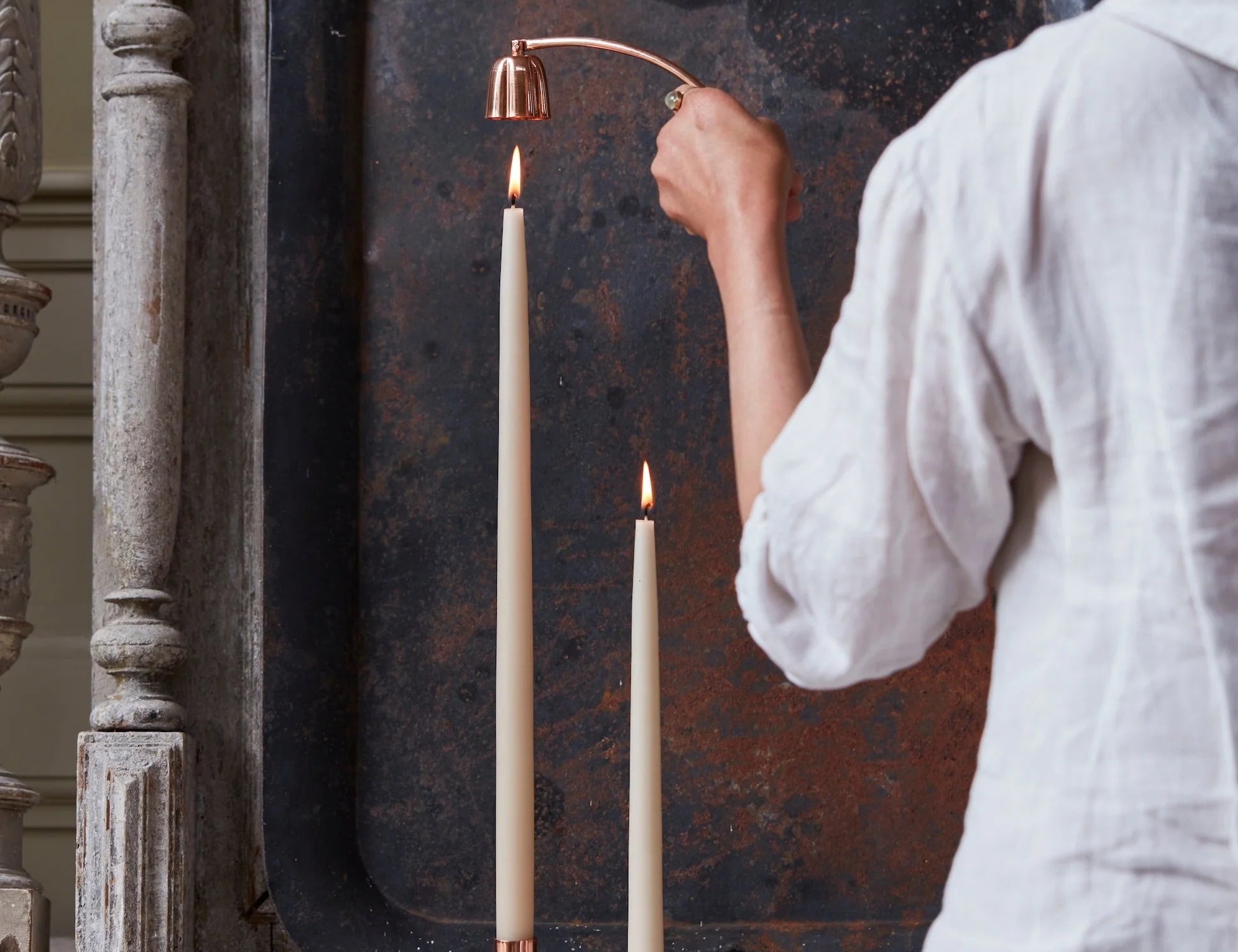 Woman in a white shirt using The Floral Society Copper Candle Snuffer on a taper candle