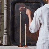 Woman in a white shirt using The Floral Society Copper Candle Snuffer on a taper candle