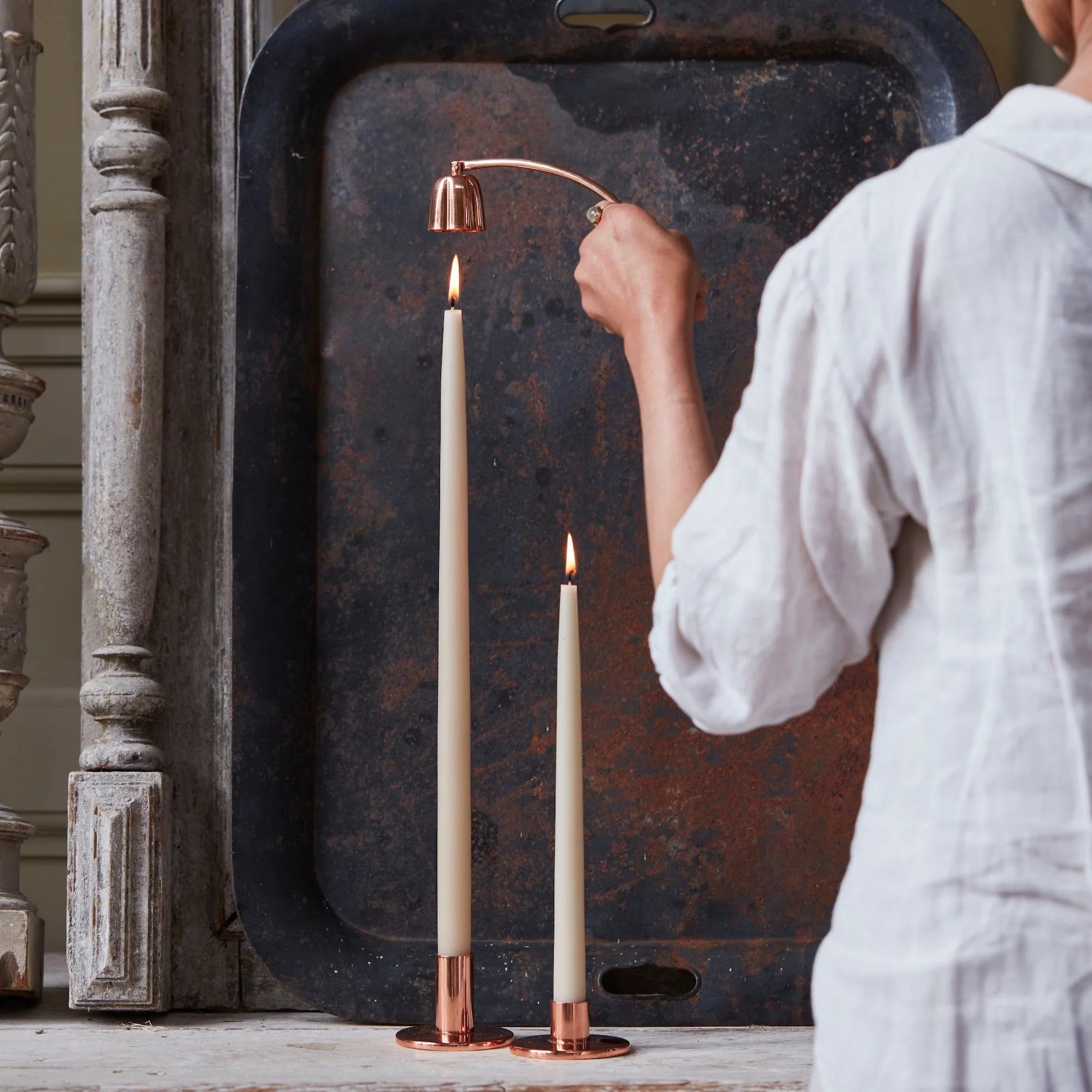 Woman in a white shirt using The Floral Society Copper Candle Snuffer on a taper candle