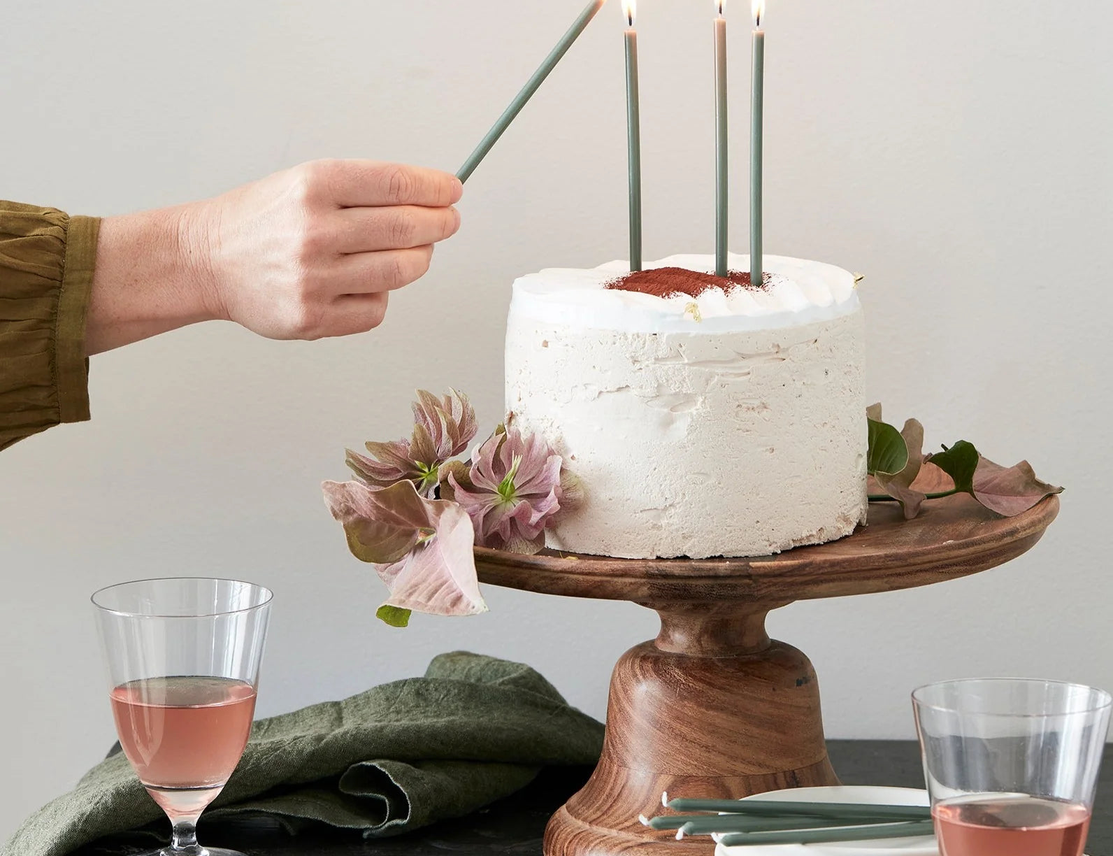 Hand lighting The Floral Society Wishing Candles in green on a white frosted cake