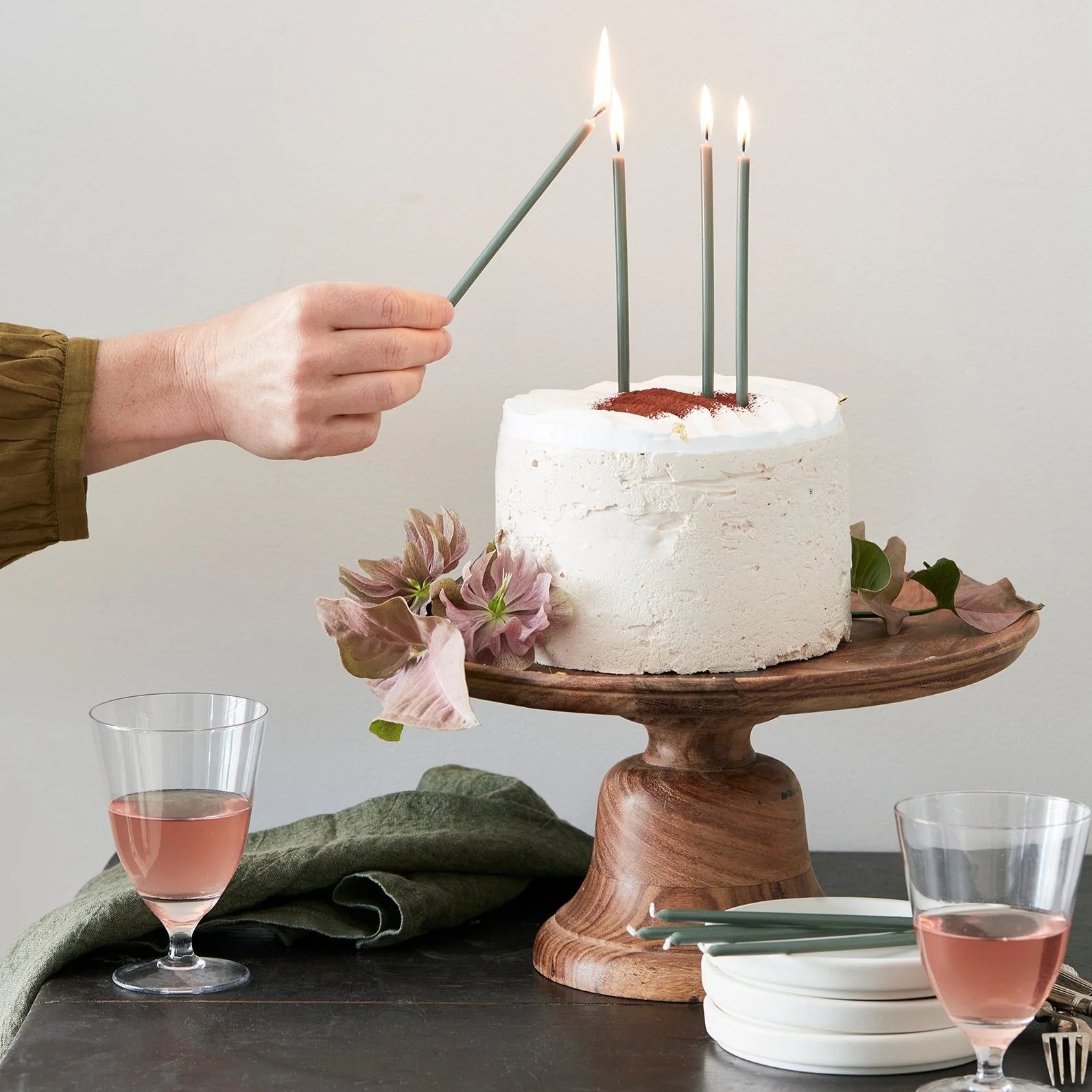 Hand lighting The Floral Society Wishing Candles in green on a white frosted cake