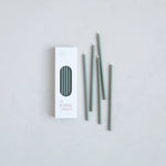 The Floral Society Wishing Candles in Moss, thin sage green taper candles beside their white box