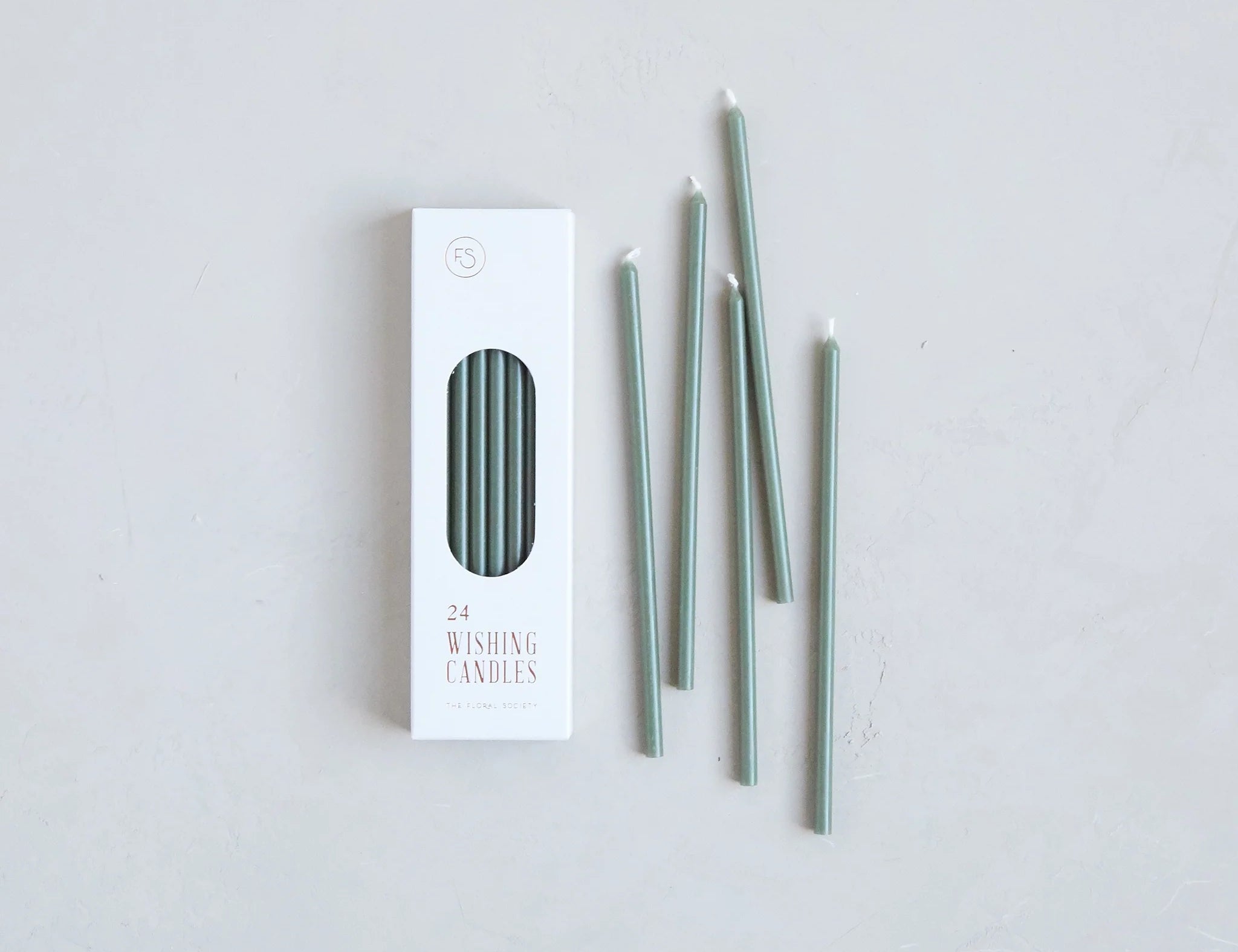 The Floral Society Wishing Candles in Moss, thin sage green taper candles beside their white box