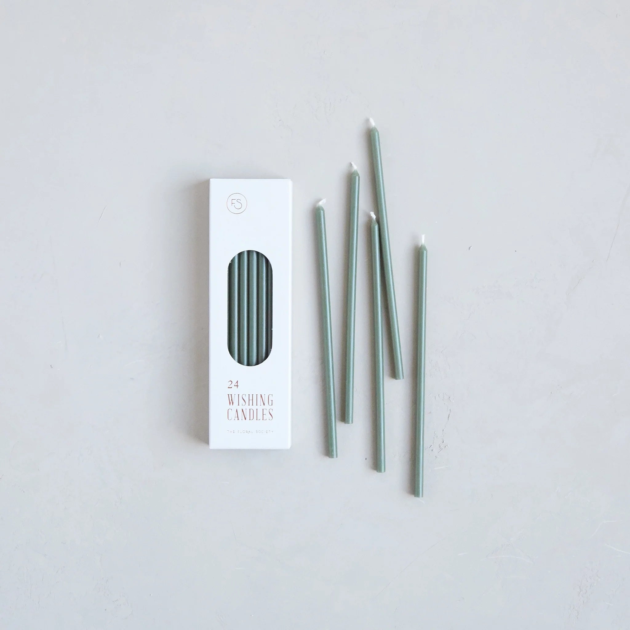 The Floral Society Wishing Candles in Moss, thin sage green taper candles beside their white box