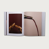 The Gospels book open to a spread with photos of a hand and pouring wine