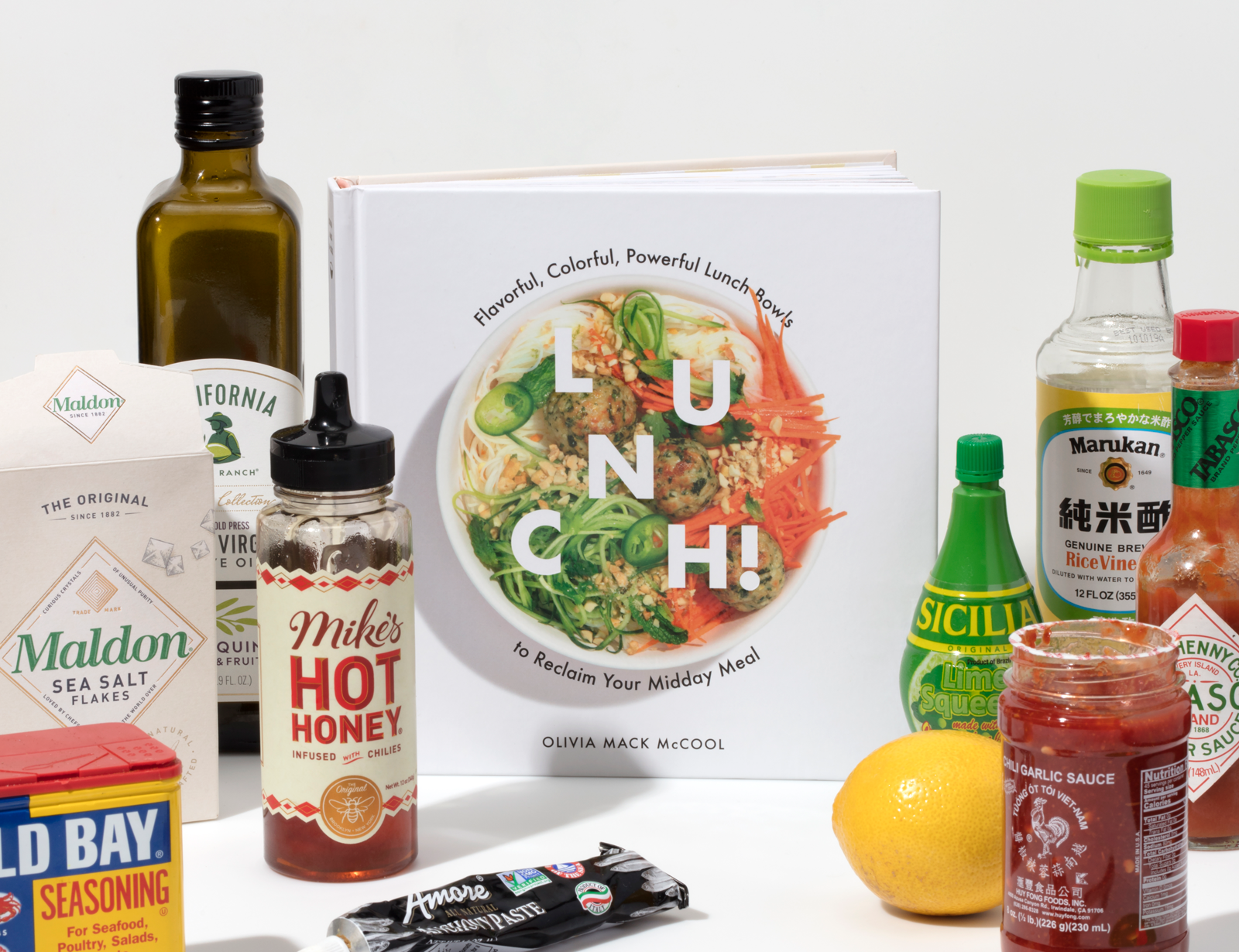 W&P Lunch Cookbook surrounded by pantry staples like hot honey, sea salt, olive oil and hot sauce