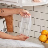 Hands stretching a W&P Reusable Stretch Lid over a glass bowl in a kitchen