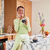 Smiling woman in green eating from a W&P Seal Tight Bowl in Terrazzo Charcoal at a marble counter